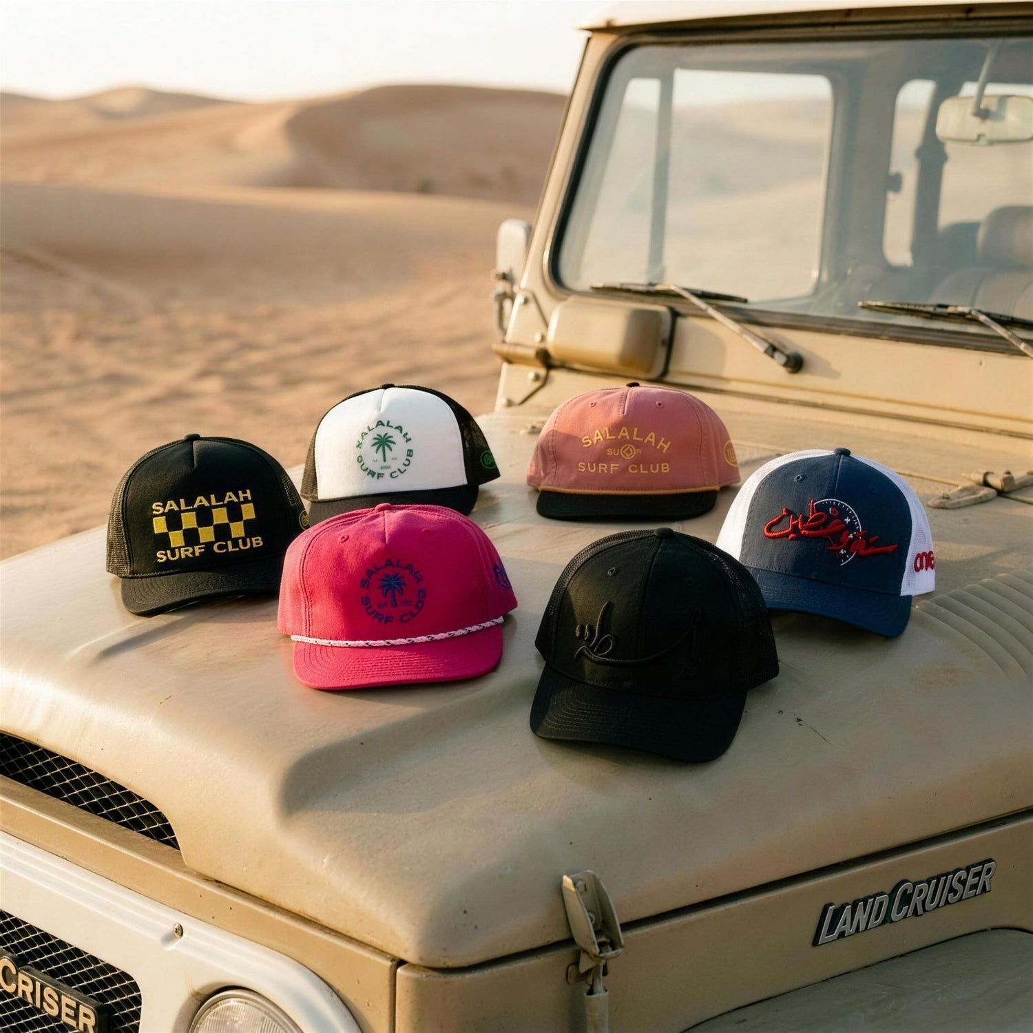 One8 Arabic trucker hats and Salalah Surf Club caps arranged on a vintage Land Cruiser hood in the desert at golden hour