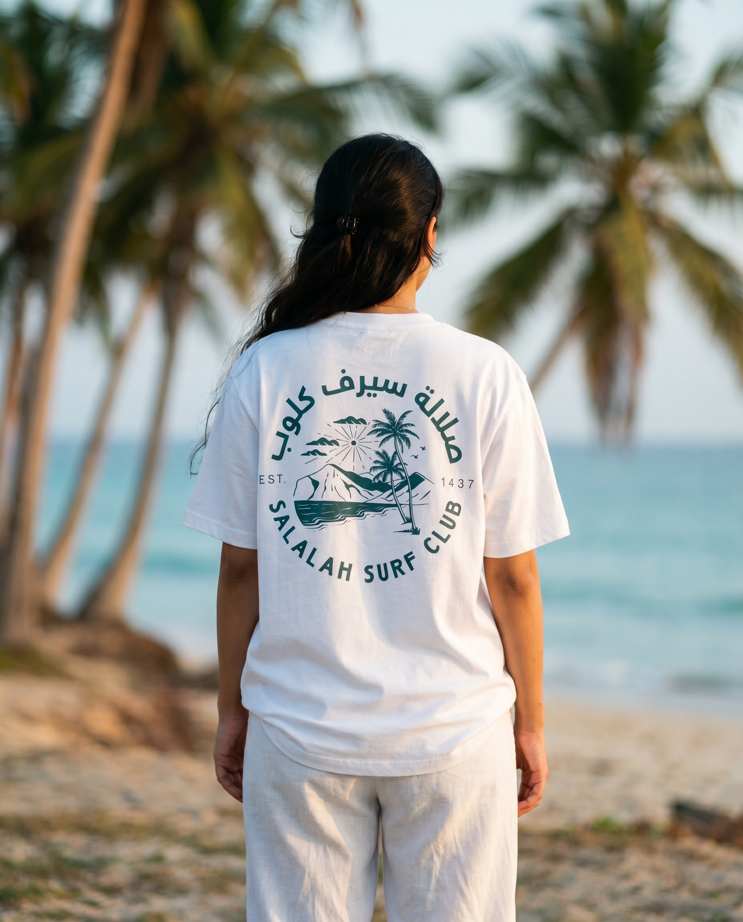 Salalah Surf Club Coconut Palms tee back print worn by female model on Salalah beach