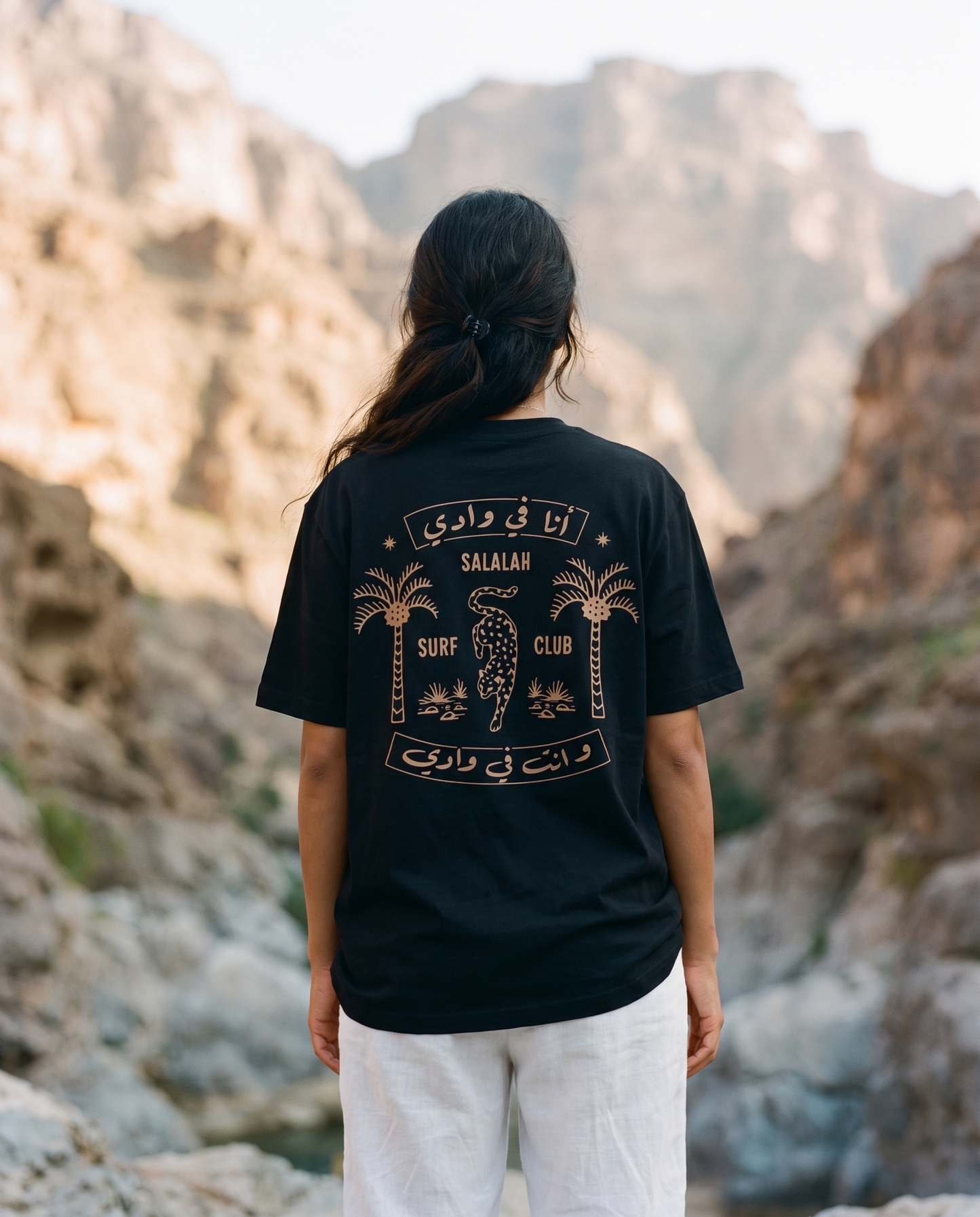 Salalah Surf Club Arabian Leopard black tee back print worn by female model in a rocky wadi