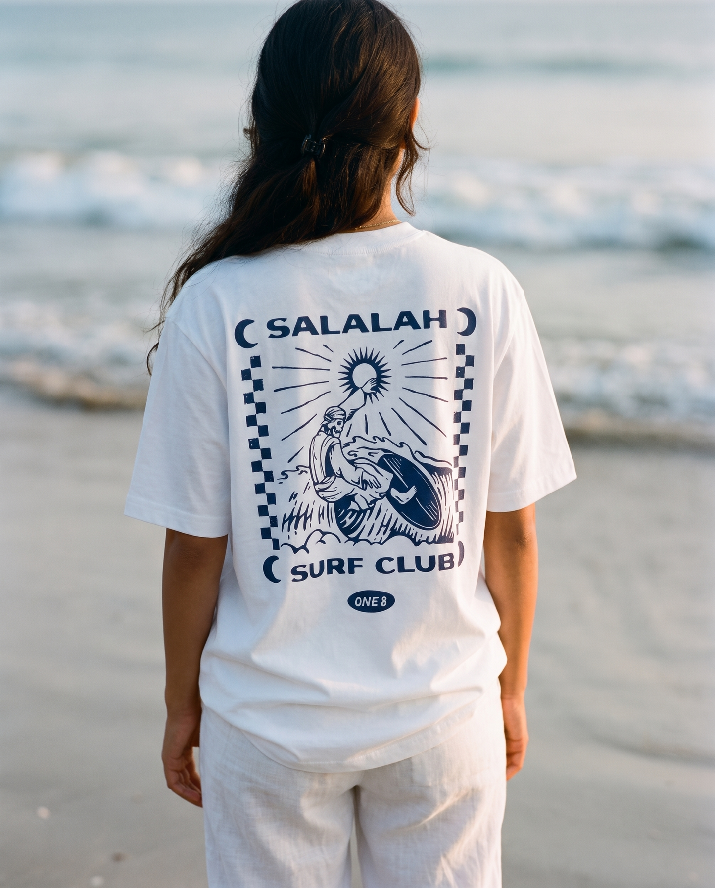 Salalah Surf Club Omani Surfer tee back print worn by female model on the shoreline