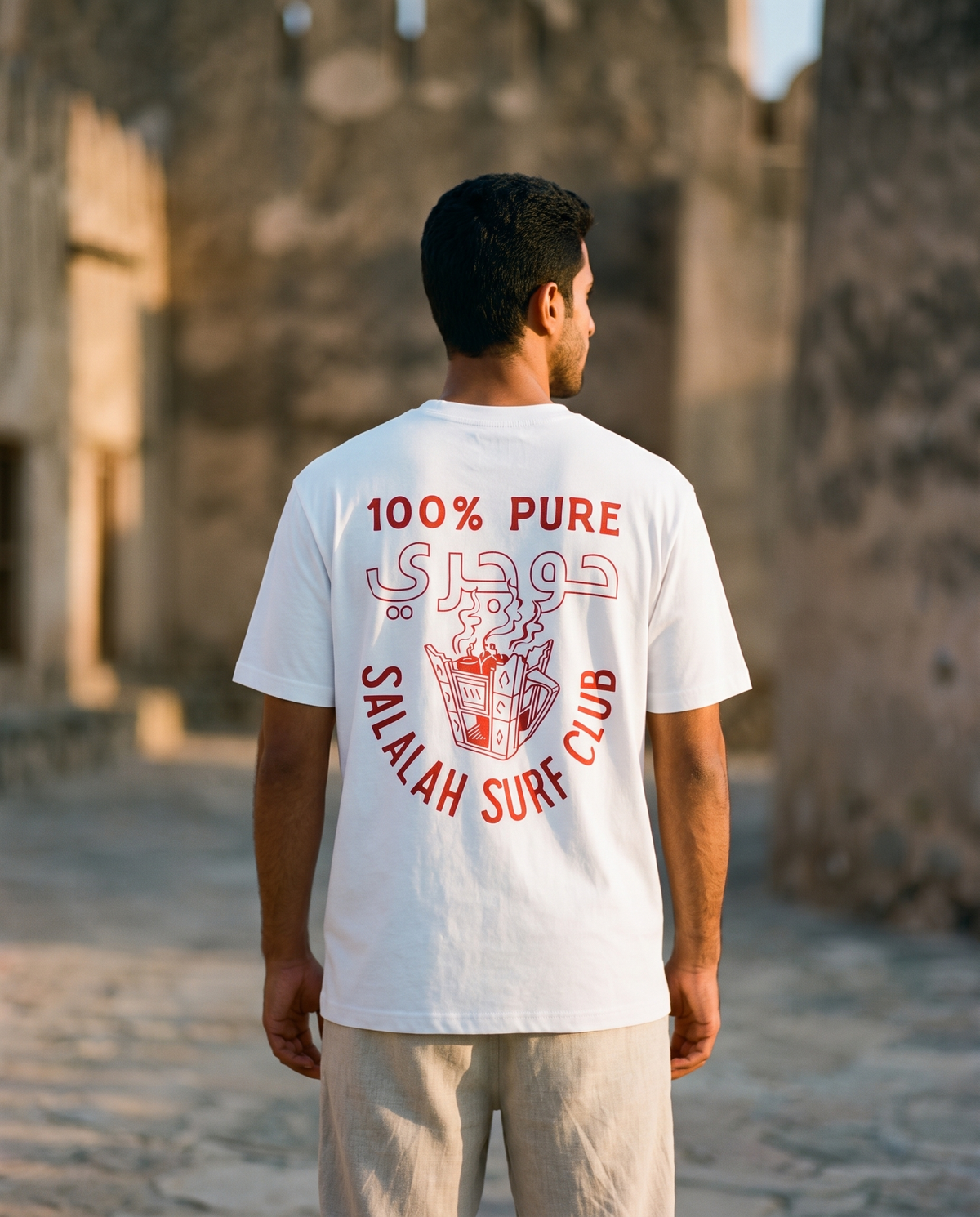Salalah Surf Club Omani Gold tee back print with incense burner, male model at Omani fort
