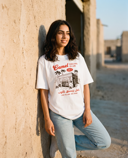 Desert Workshop Camel Racing Club tee, female model at village garage wall