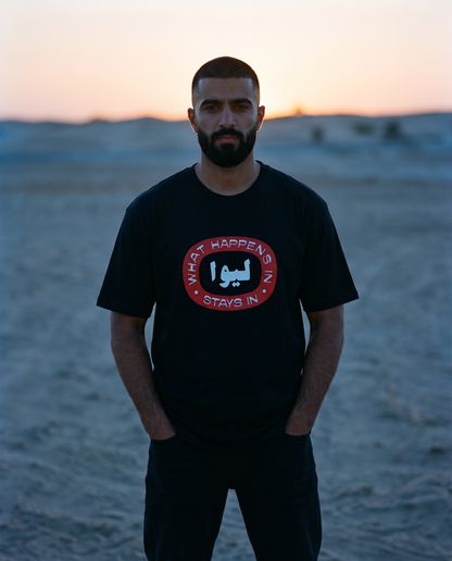 What Happens in LIWA black tee front print, male model in dunes at dusk