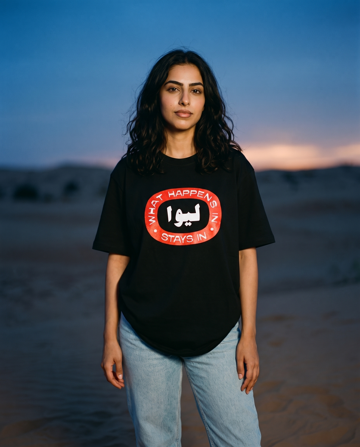 What Happens in LIWA black tee front print, female model in dunes at dusk
