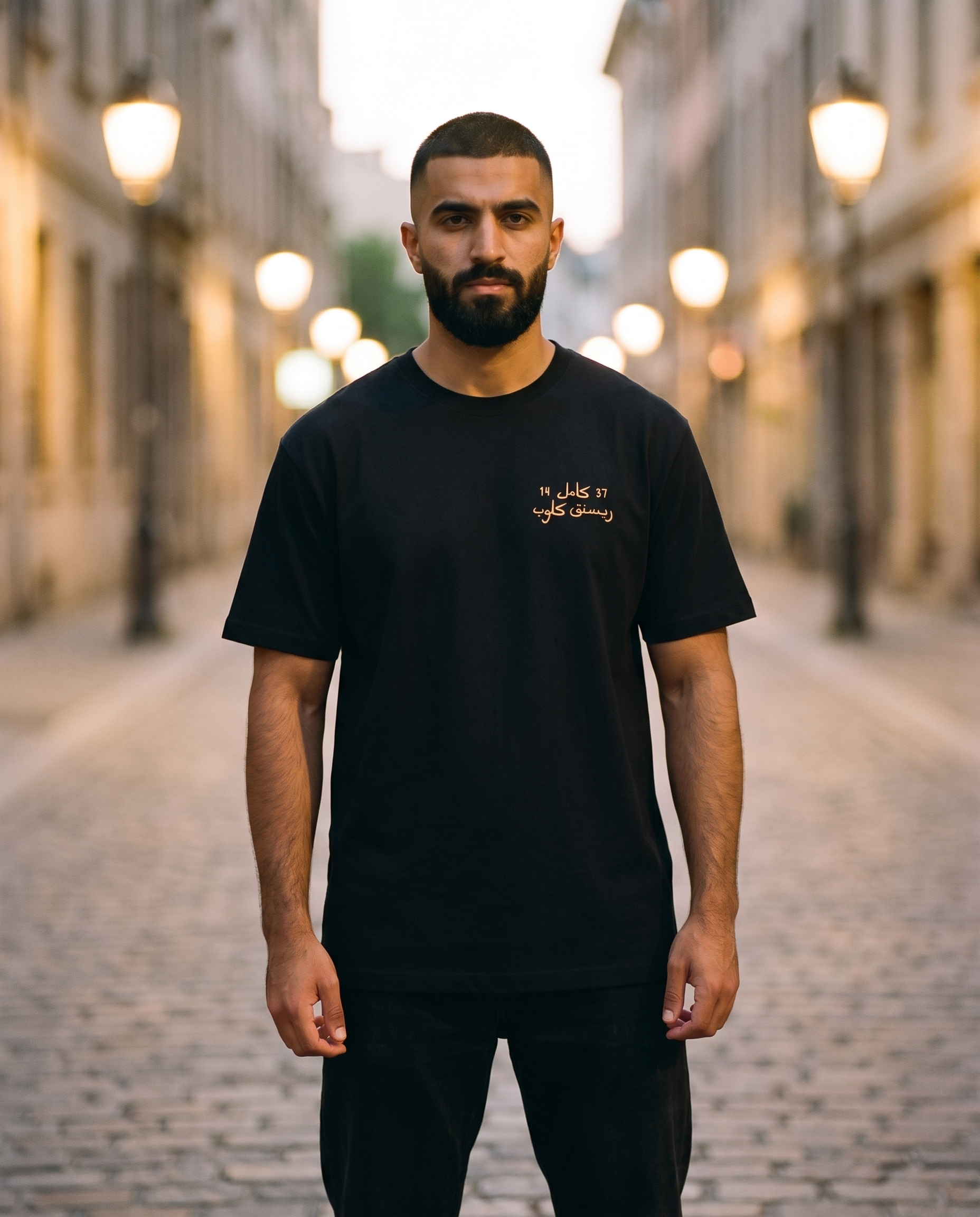 Million Street Tee gold Arabic chest print worn by male model on a lamplit street at dusk