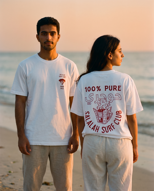 Omani Gold tee worn by male and female models on a golden-hour beach, front and back view