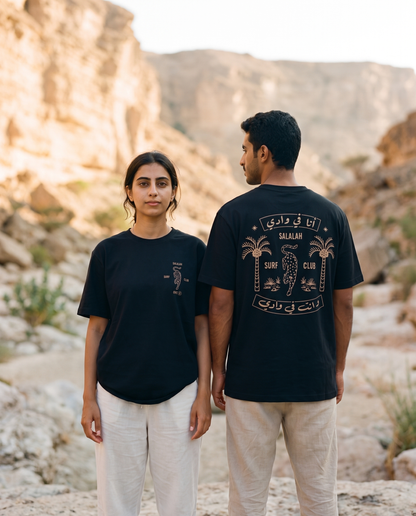 Leopard tee in black worn by male and female models in a rocky wadi, front and back view