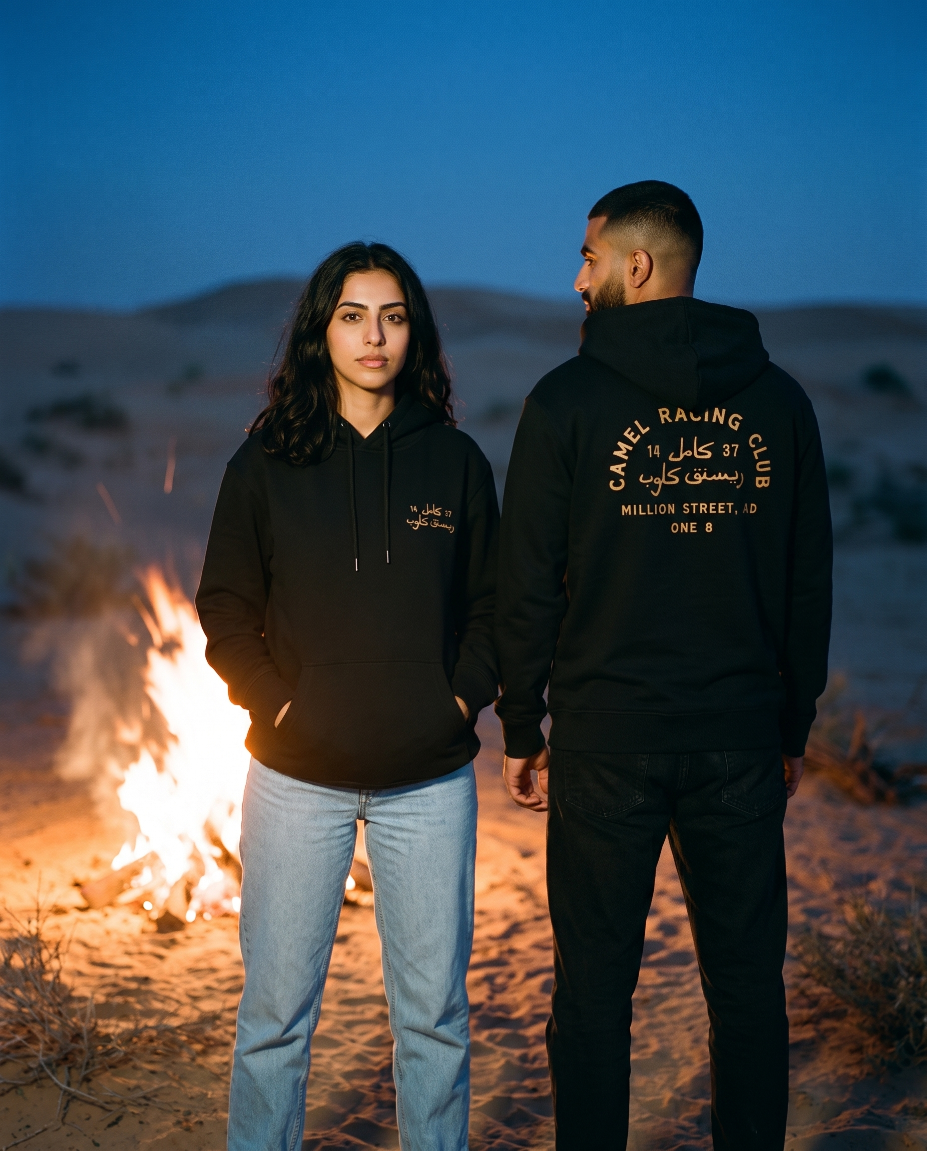 Camel Racing Club Arabic hoodie worn by male and female models by a desert campfire, front and back view