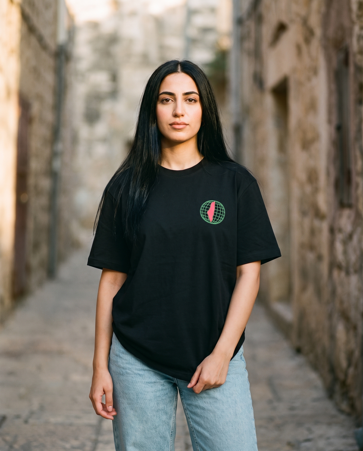 Free Palestine black tee globe chest print worn by female model in an old stone alley