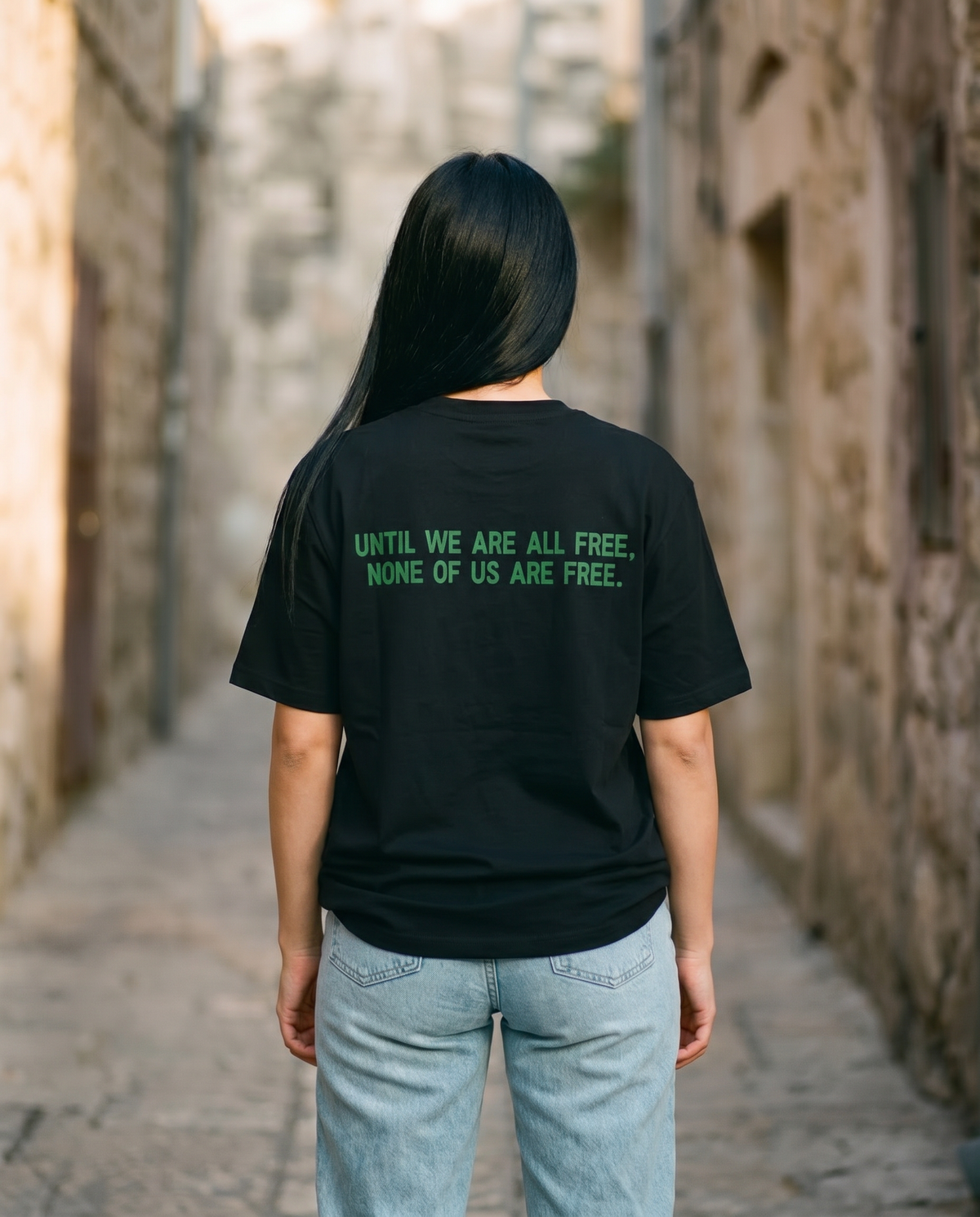 Free Palestine black tee back print worn by female model in an old stone alley