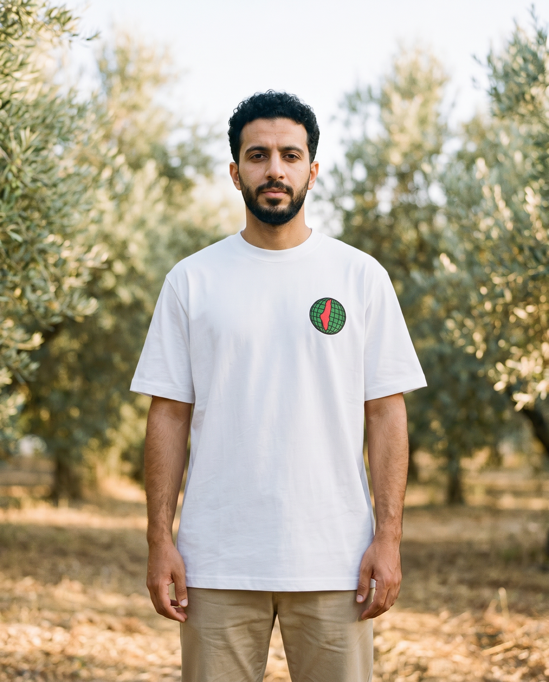Free Palestine white tee globe chest print worn by male model in an olive grove