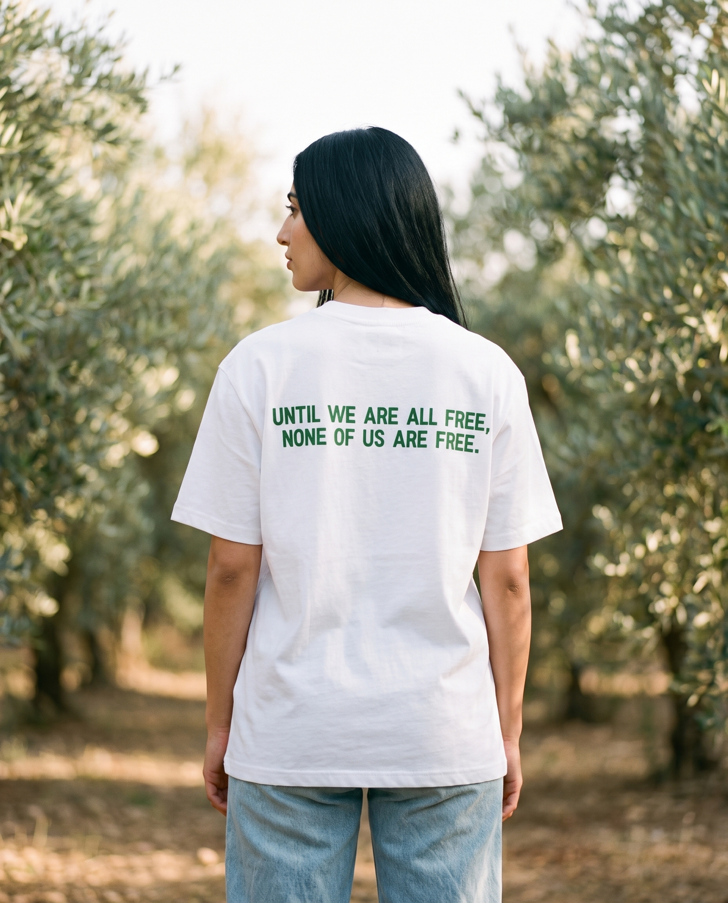 Free Palestine white tee back print worn by female model in an olive grove