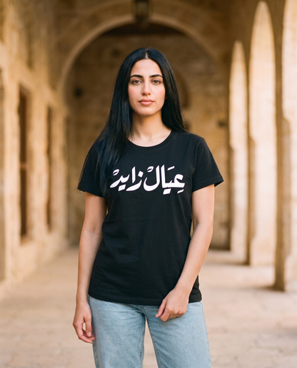 A'yal Zayed heritage ladies tee white Arabic calligraphy worn by female model in a heritage courtyard