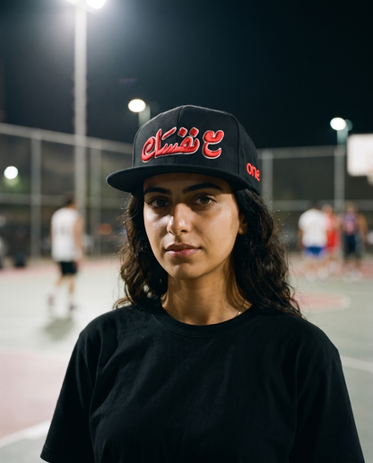 Ma'a Nafsak black flat brim snapback worn frontwards by female model at a night streetball court