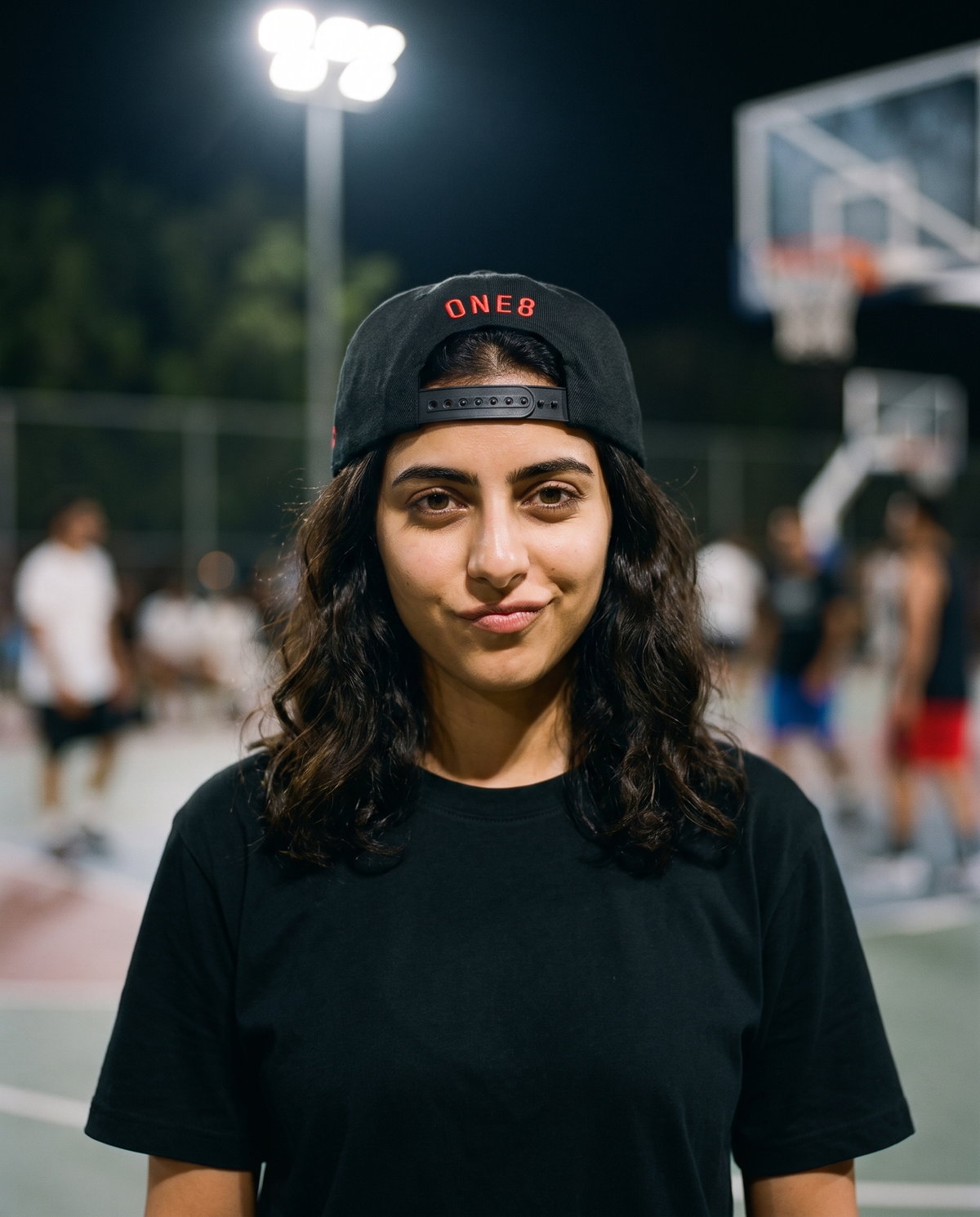 Ma'a Nafsak snapback worn backwards showing ONE8 back, female model on floodlit court