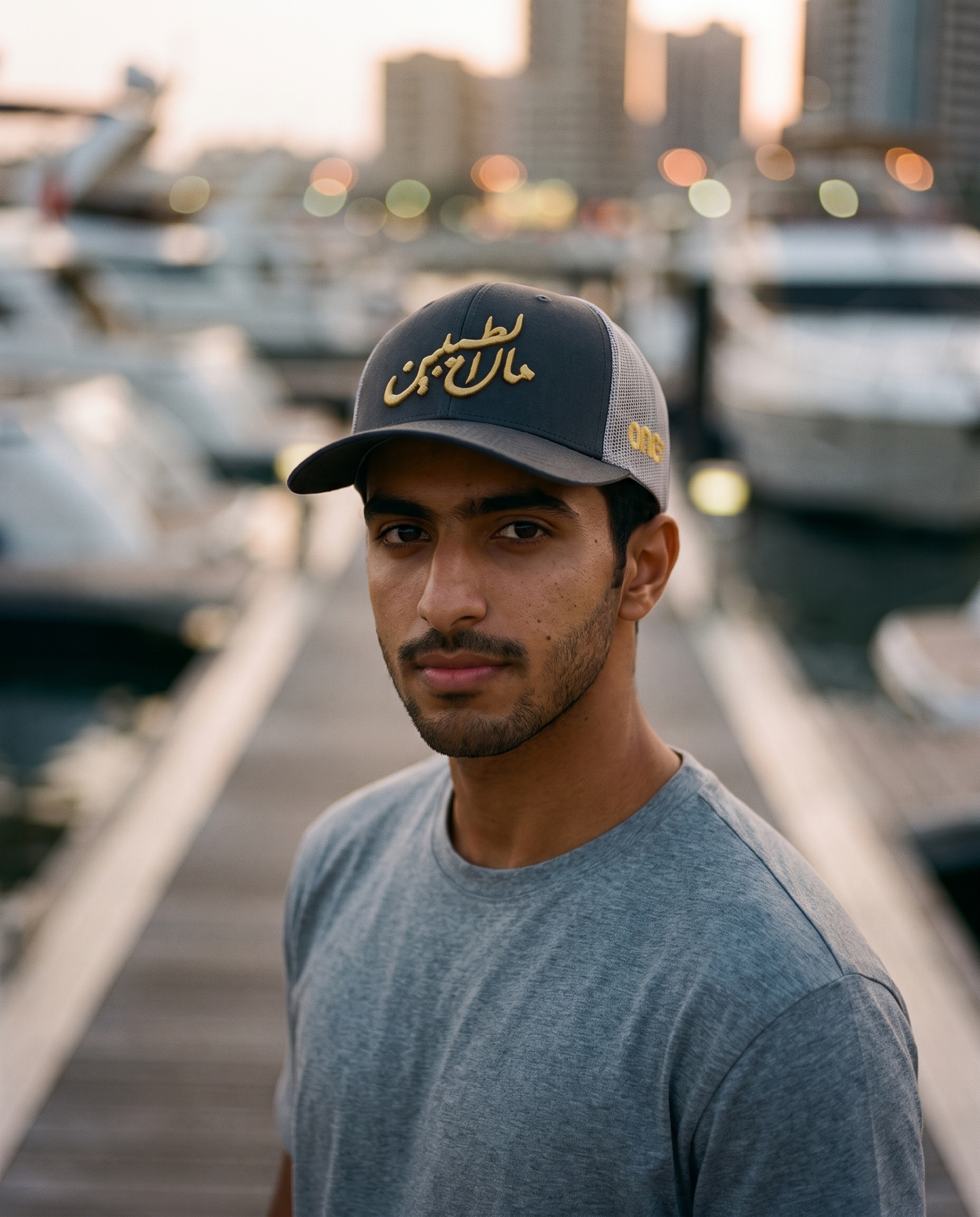 Mal Al Tayyebeen curved brim trucker worn frontwards by male model at a marina at dusk